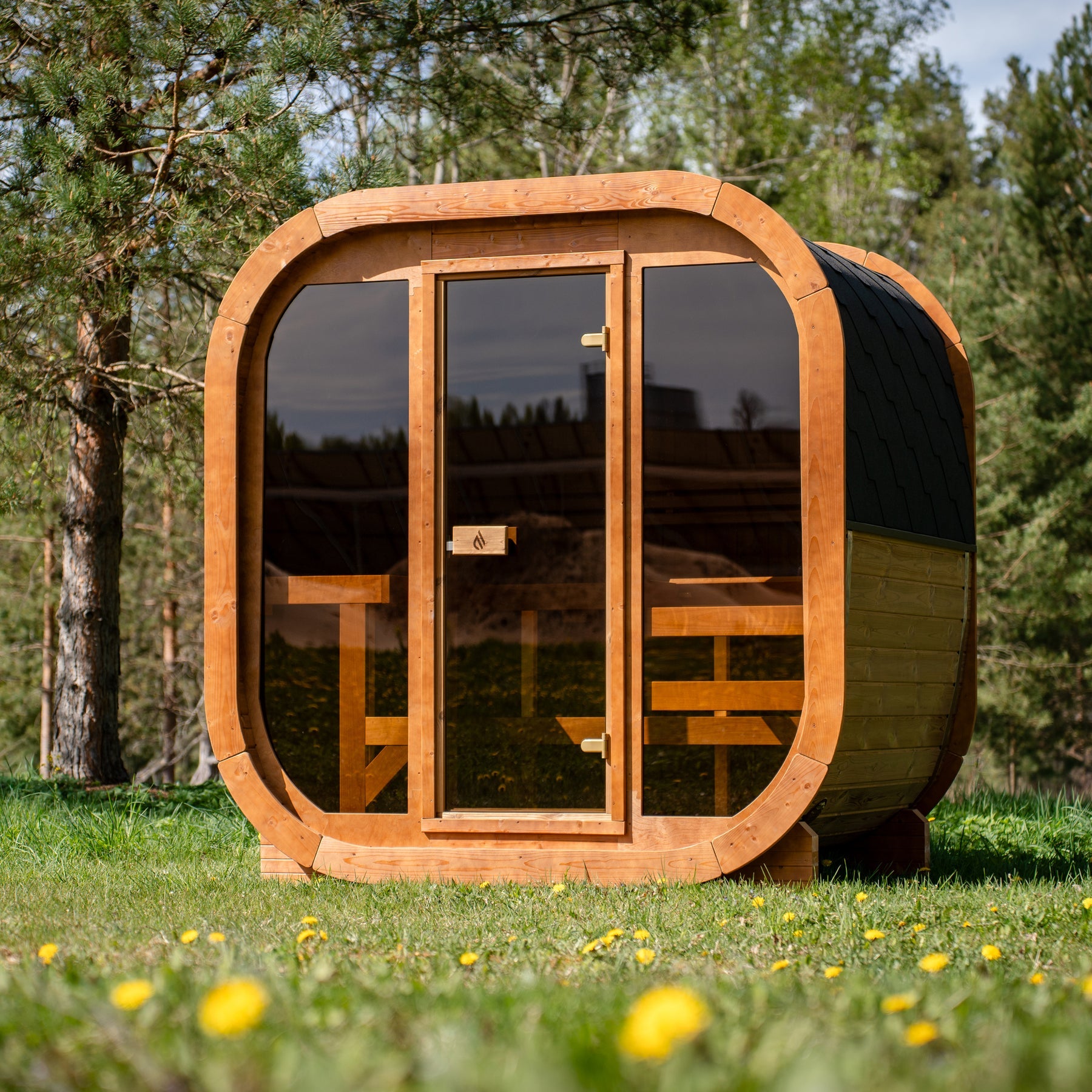 PlusLife Max Traditional 2.0 outdoor sauna: rounded-square timber cabin with a full tinted-glass front, centred glass door, black shingle roof and timber cradle feet