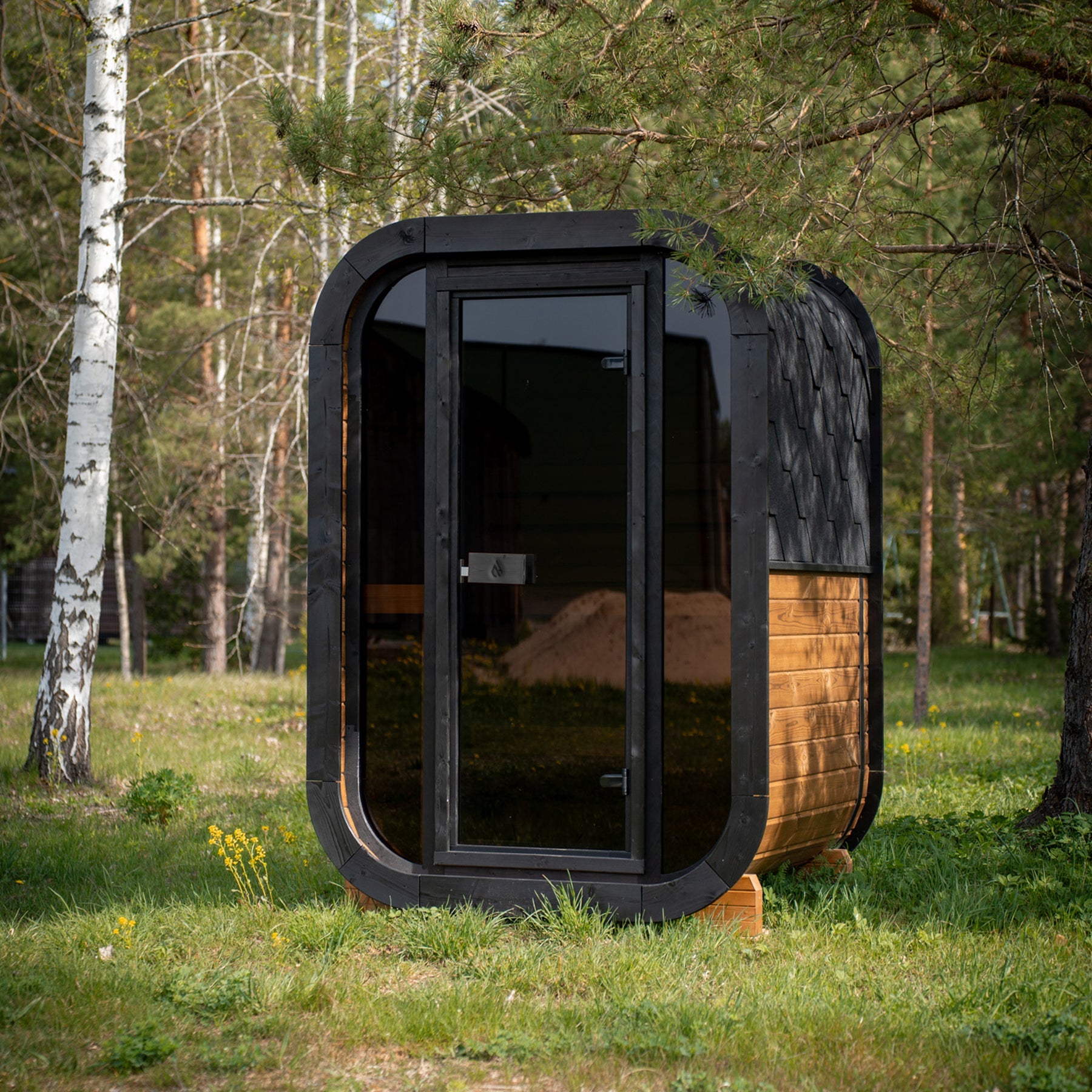 PlusLife Mini Traditional 2.0 outdoor sauna: compact timber cabin with a tinted-glass door, black shingle roof and timber cradle feet
